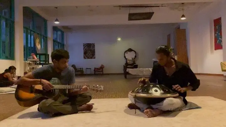 Two musicians playing guitar and handpan on the floor