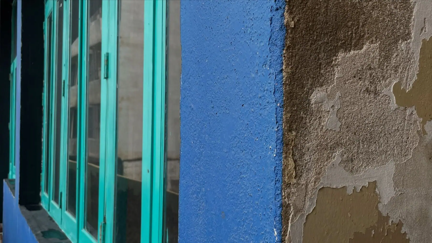 Teal window frames against a blue wall and weathered plaster
