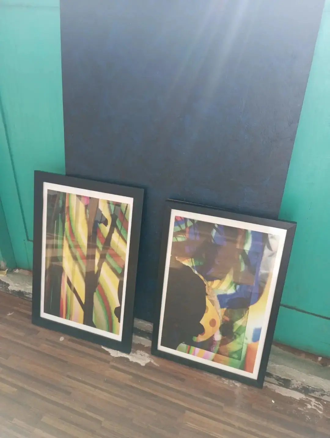 Two framed works leaning against a teal wall